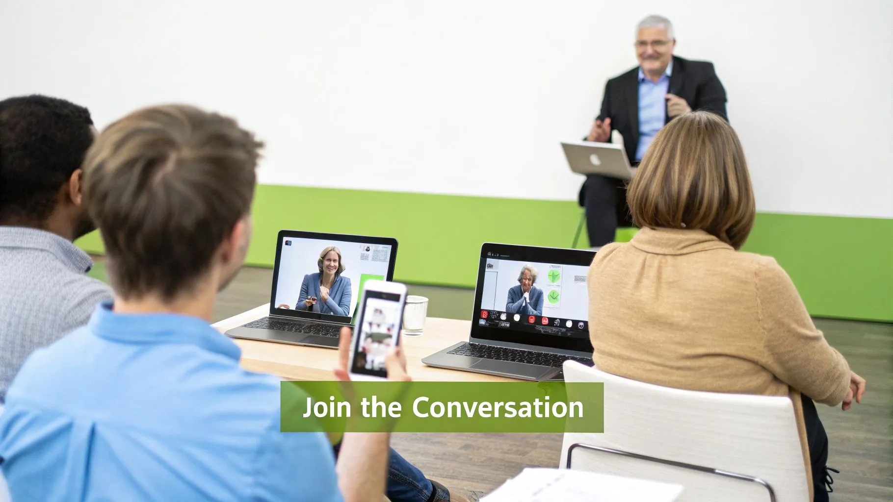 Attendees at a town hall event, engaging with an in-person speaker and virtual participants on screens.