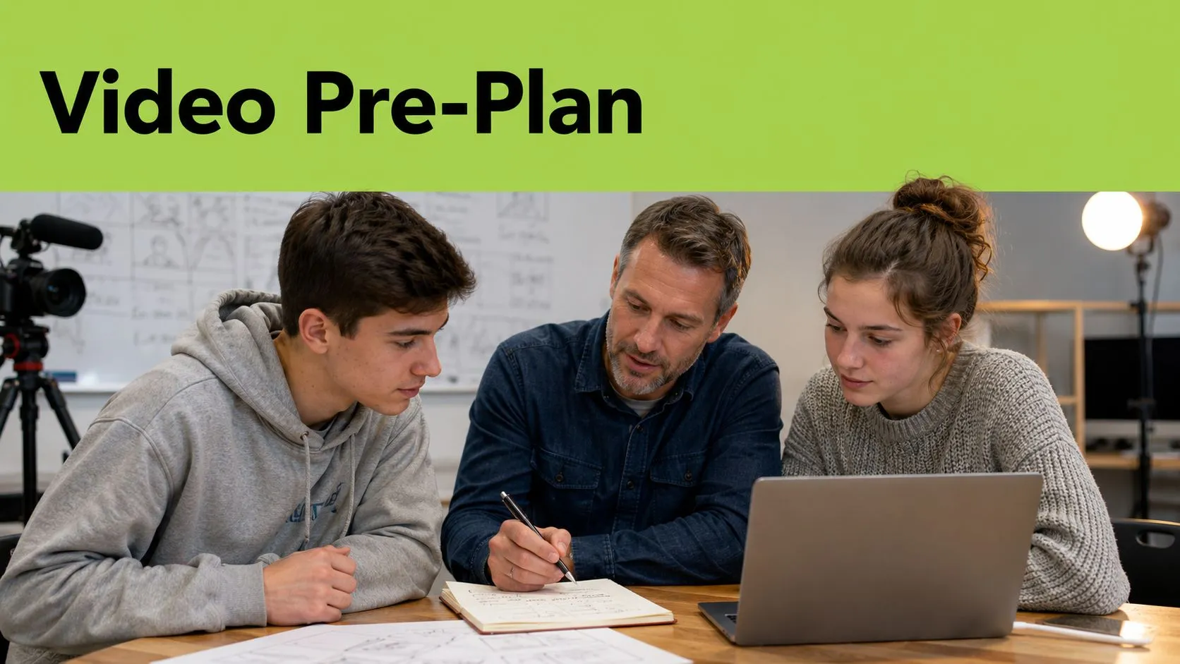 A teacher helps two students plan a video production project using a laptop and storyboard notes.